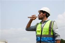 A construction worker takes a drink from a plastic water bottle on a hot day.
