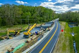 Aerial view of expanding a two-lane road to a four-lane highway with heavy construction equipment such as cranes parked for the weekend before a small bridge is completed in Maryland USA