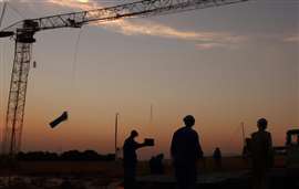 Workers and cranes silhouetted against a sunset