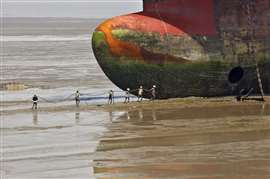Workers on a beach with a giant cargo vessel