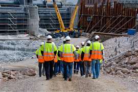 A group of construction workers with their backs to the camera walk onto a construction site