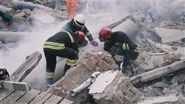 Three emergency workers wearing hard hats sift through rubble after an earthquake