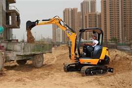 A JCB mini excavator loads a trailer on a construction site in India