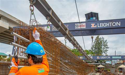 A Leighton Asia worker in an orange hi-vis vest and hard hat guides steel reinforcements into place