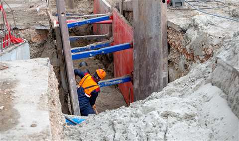 A worker digging in a trench with shoring protection